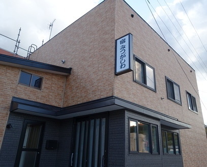 A modern two-story building features a combination of brick and dark-colored exterior walls. Large windows allow natural light to enter. The entrance is framed by sliding glass doors, providing easy access. An exterior sign indicates the name of the establishment, displayed prominently above the entrance.