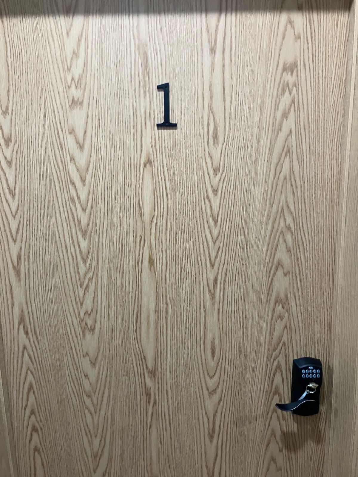 A wooden door with a natural grain finish is featured, displaying the number "1" prominently. A keyless entry system is located on the right side of the door, offering convenient access.