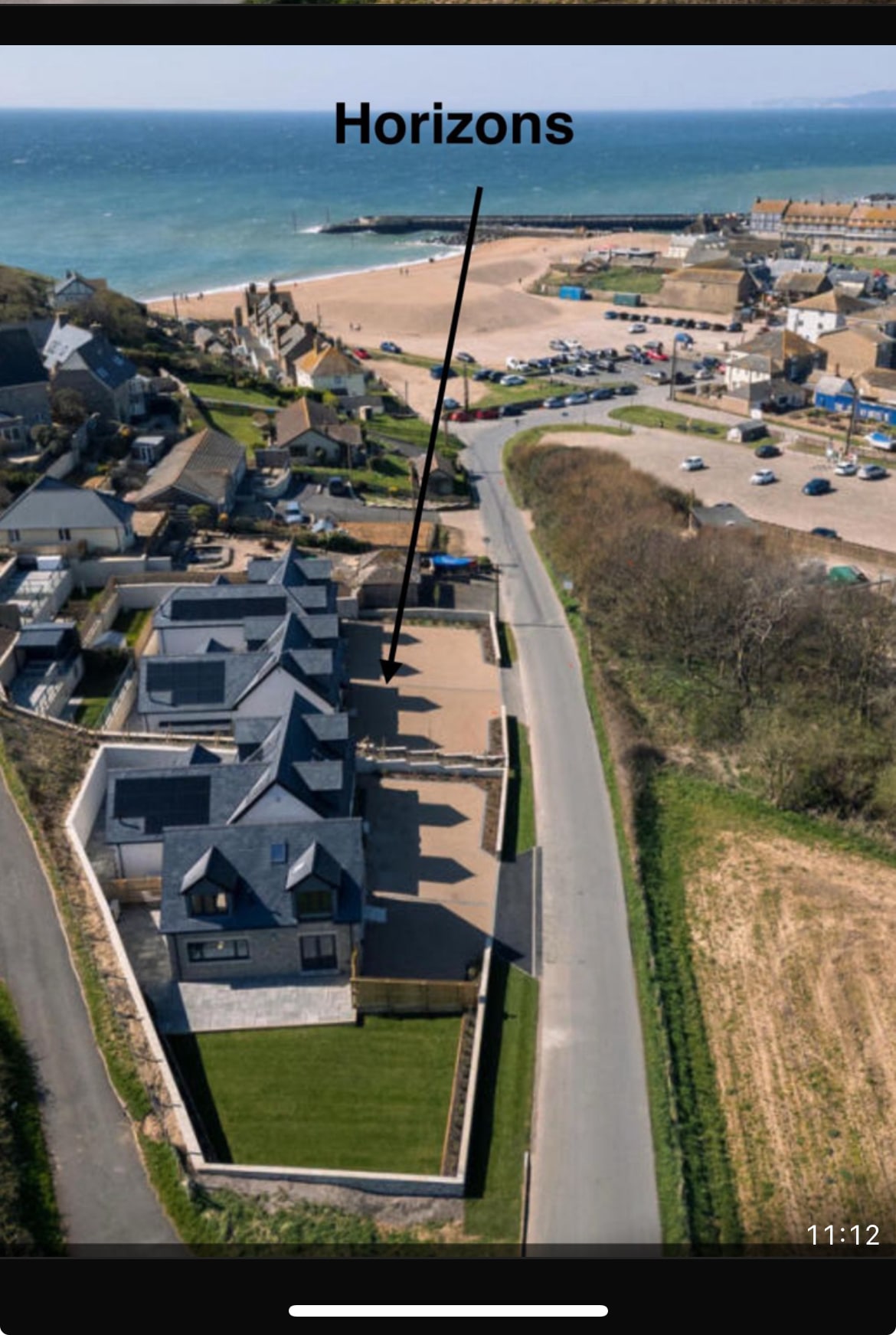 An aerial view presents the 'Horizons' property, with multiple newly built homes surrounded by landscaped gardens. The coastline is visible nearby, along with the sandy beach and the harbor area. A paved road leads towards the property, enhancing the accessibility.