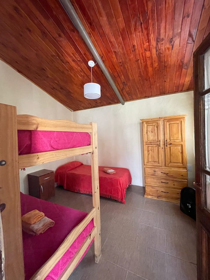 Dormitorio acogedor con techo de madera y detalles cálidos. Equipado con camas cómodas y mobiliario rústico, ideal para descansar y disfrutar de un ambiente familiar y relajado.