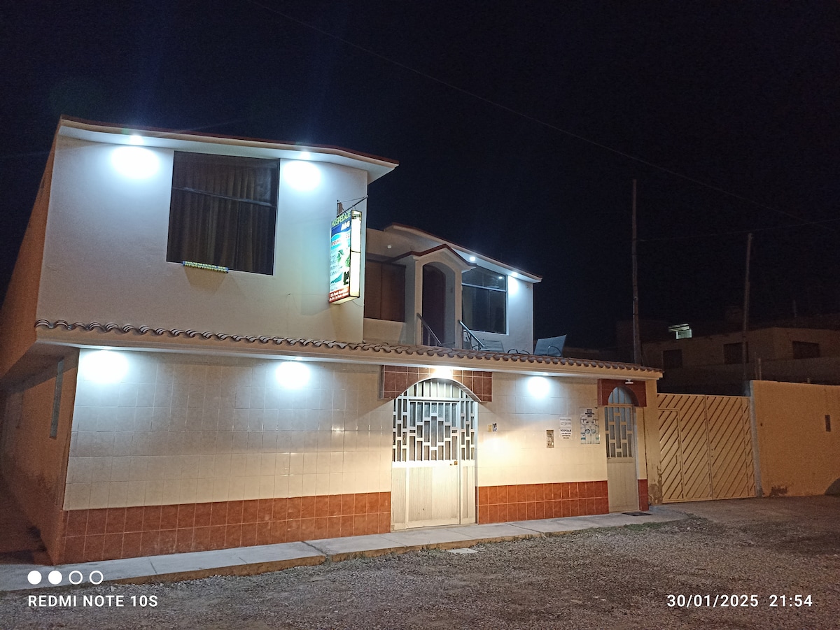 The two-story building is illuminated at night, showcasing a well-lit exterior with bright lights. The architecture features a combination of light-colored walls and a tiled lower section, while large windows provide a welcoming appearance.
