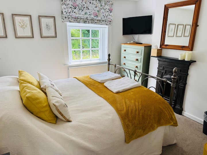 Una estructura de cama metálica de estilo tradicional con sábanas de algodón egipcio y ropa de cama de plumas complementa la chimenea de estilo victoriano.  Un televisor inteligente se suma a tu sensación de lujo.