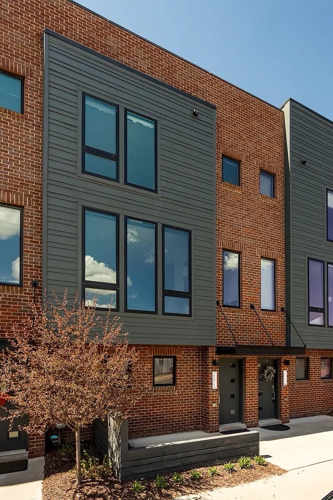 The multi-level townhome features a modern exterior characterized by large, rectangular windows that allow natural light to enter. The facade combines brick and contemporary siding, while a small front entrance with steps is visible, inviting guests into the space.