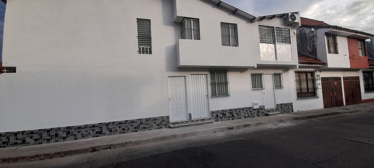 The exterior of the accommodation features a clean, white facade with a combination of windows and doors. A mix of textures is present with a stone base. The street-side view highlights a simple yet functional design, maintaining a welcoming appearance.