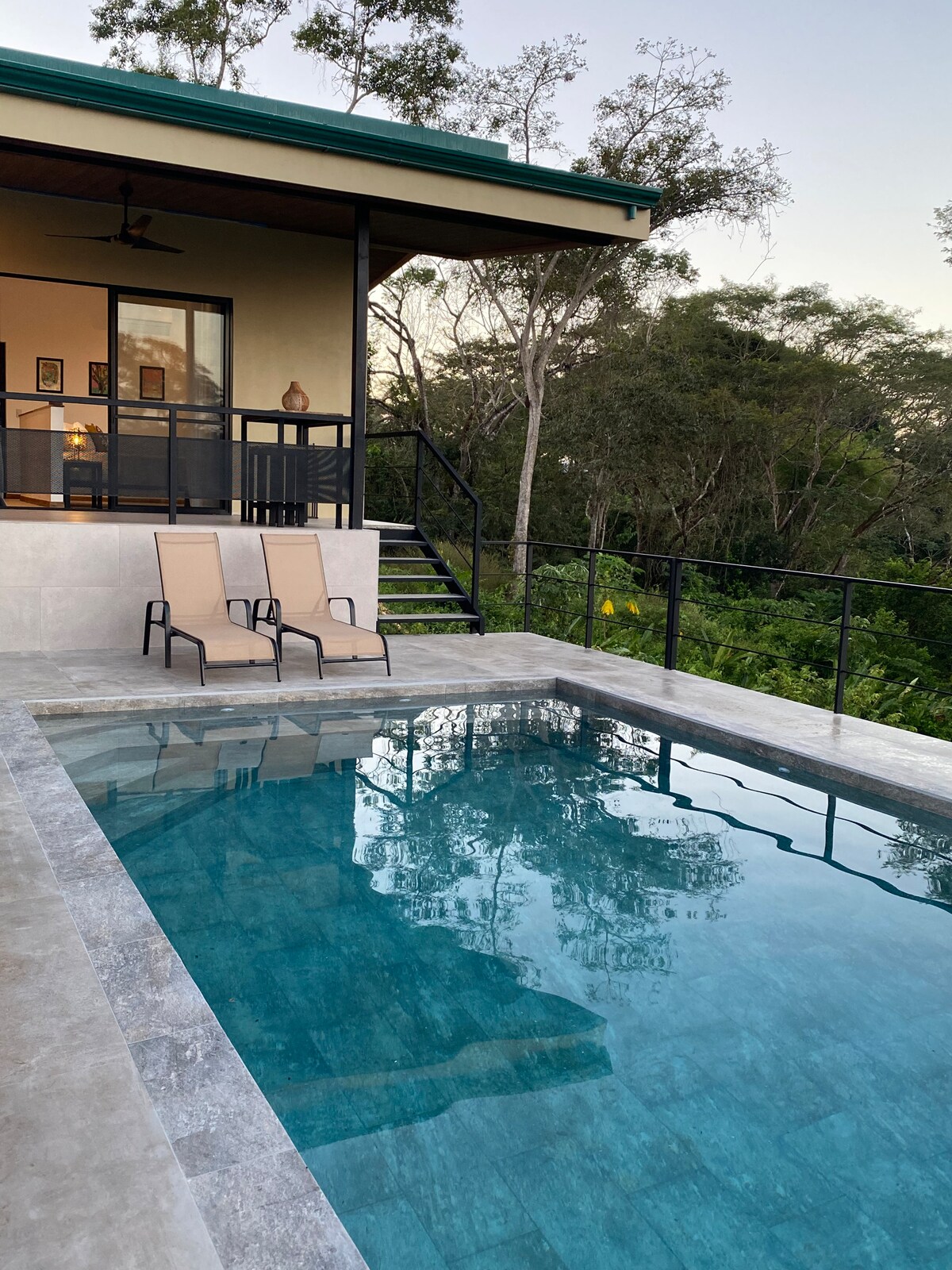 A private terrace features a small pool, with light reflecting off its clear water. Two lounge chairs are positioned beside the pool, offering a tranquil setting surrounded by lush greenery and trees, with the residence visible in the background.