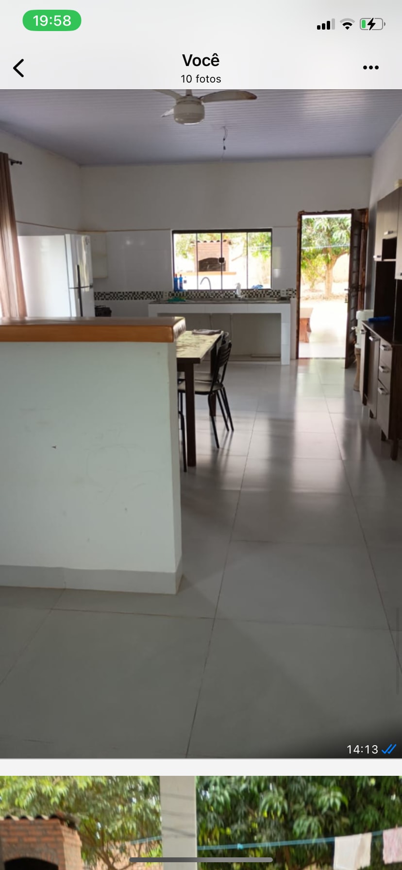 A spacious kitchen area is visible, featuring a central island with seating around it. Large windows allow natural light to illuminate the space, while modern cabinetry and appliances provide convenience. The tile flooring adds to the open and airy feel of the environment.