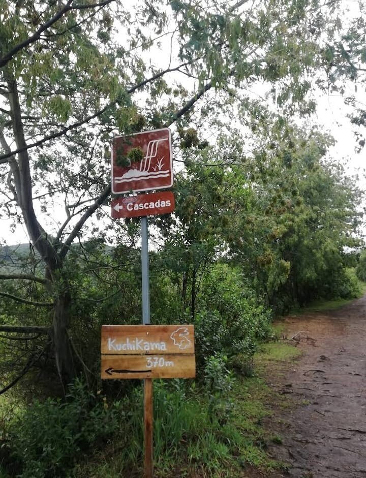 A directional sign is situated along a path surrounded by greenery, indicating the way to Cascadas and Kuchikärna, which is 370 meters ahead. A tree canopy provides a natural frame to the scene, enhancing the sense of being in a tranquil outdoor setting.