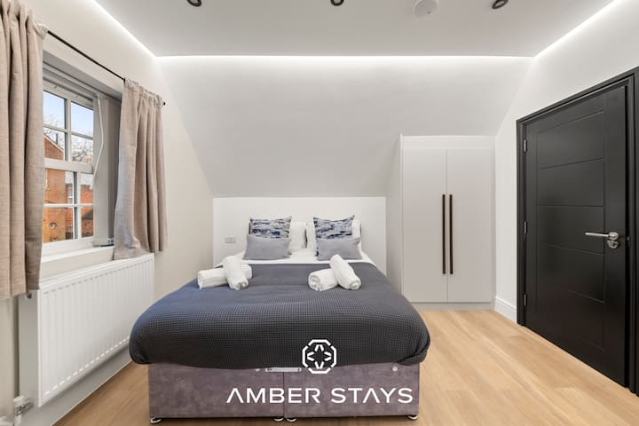 חדר שינה שחור-לבן מואר ומזמין עם מיטה נוחה, כיסא נעים ומקום שקט שבו אפשר להירגע ולהרגיש בבית.