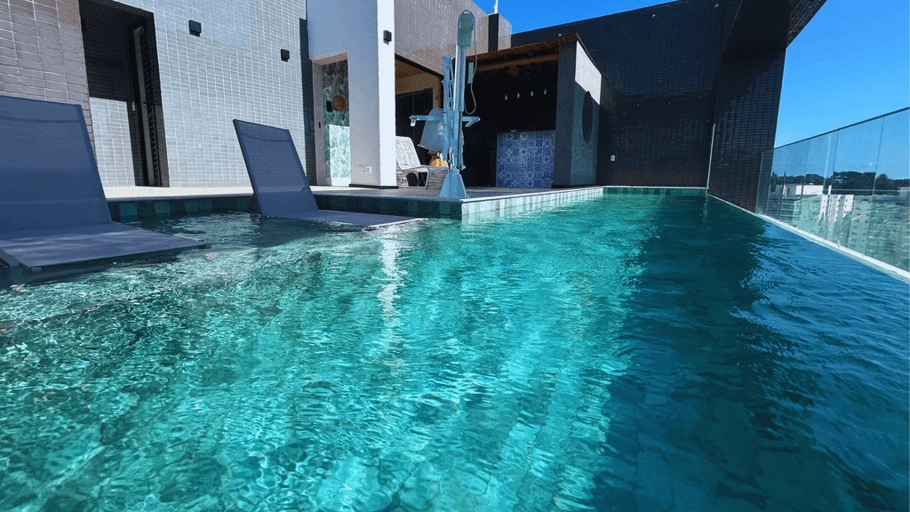A rooftop pool is revealed with clear turquoise water reflecting sunlight. Two lounge chairs are positioned along the pool edge, surrounded by a modern architectural backdrop that enhances the serene atmosphere.