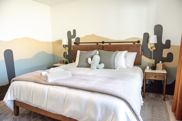 Chumba cha Jangwa Kuamka kilichozungukwa na haiba ya Arizona katika chumba cha kulala cha kifalme cha mtindo mahususi, kilicho na matandiko yenye starehe na ukuta wa taarifa ambao huleta jangwa ndani ya nyumba.