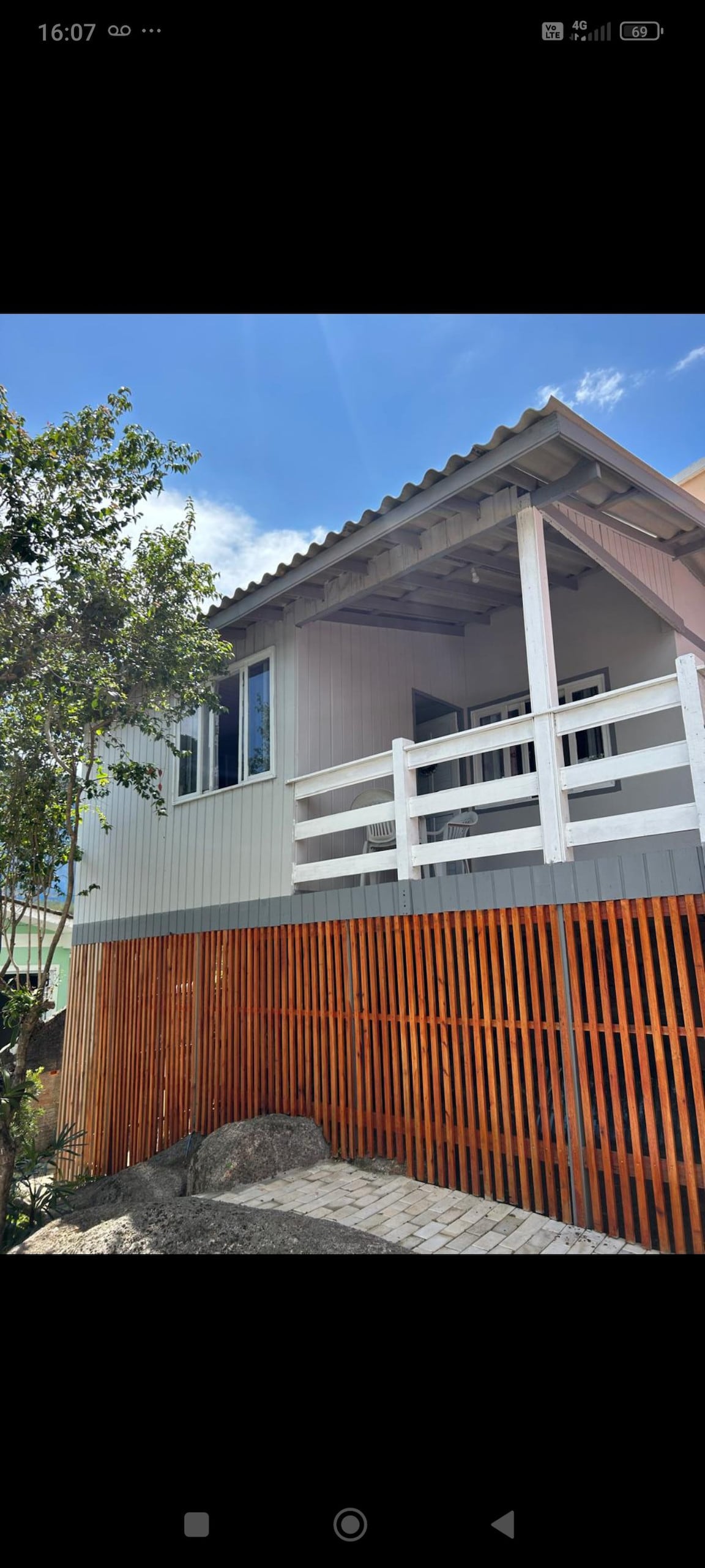 The exterior of a charming house is highlighted, showcasing a raised deck with white railings. Large windows allow natural light to enter, while a wooden fence defines the property boundary. Lush greenery surrounds the structure, contributing to a serene atmosphere.