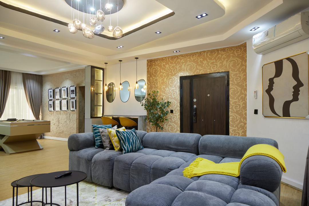 A modern living area features a large sectional sofa adorned with colorful cushions. A stylish coffee table is positioned in front, while a warm yellow throw adds a vibrant touch. Wall art and circular mirrors enhance the interior, accompanied by soft overhead lighting.