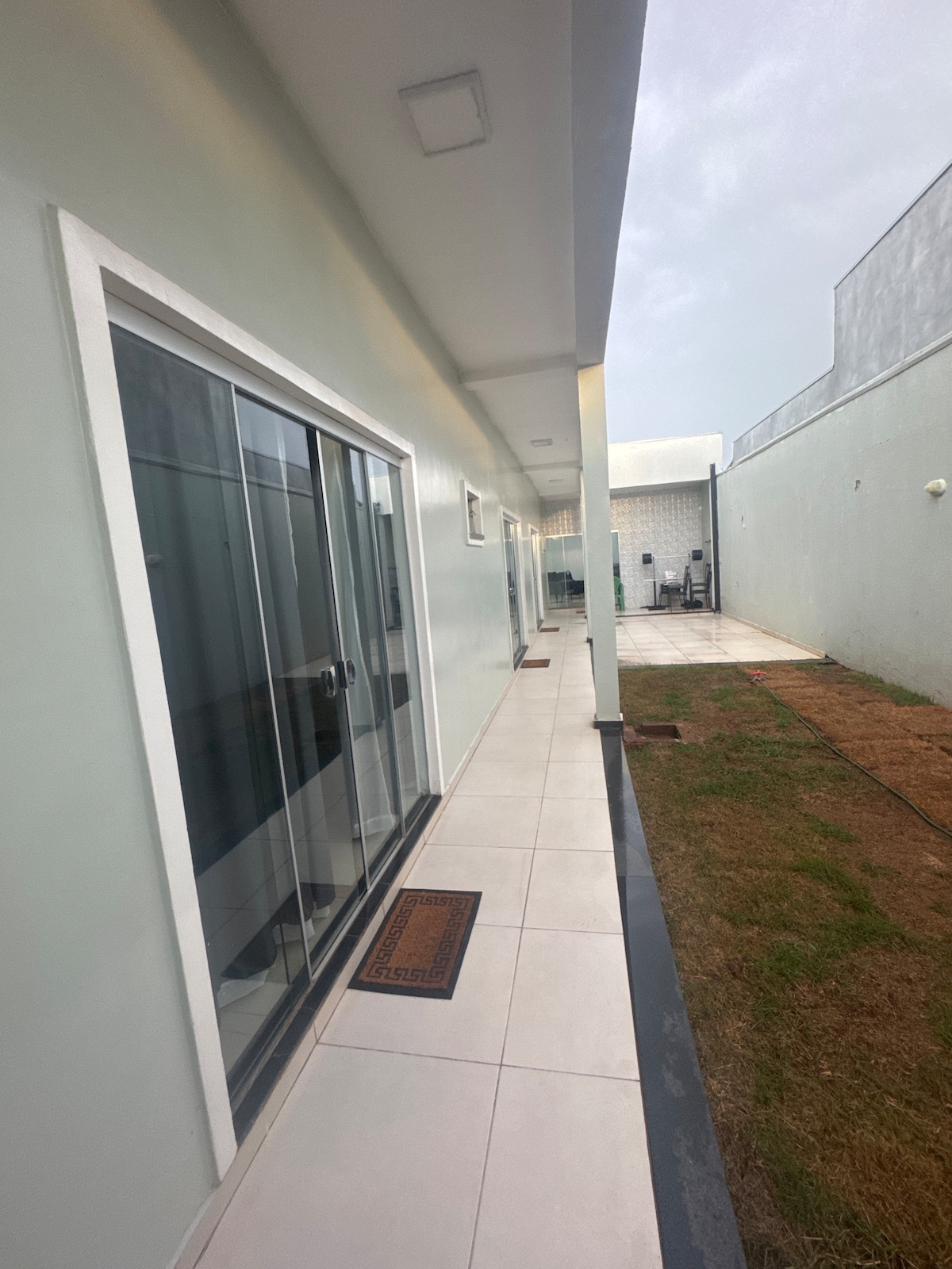 A clean, modern corridor is presented with sliding glass doors leading to private suites. The tiled floor extends alongside the building, while a small patch of grass is visible at the edge, creating a sense of privacy and space in the environment.