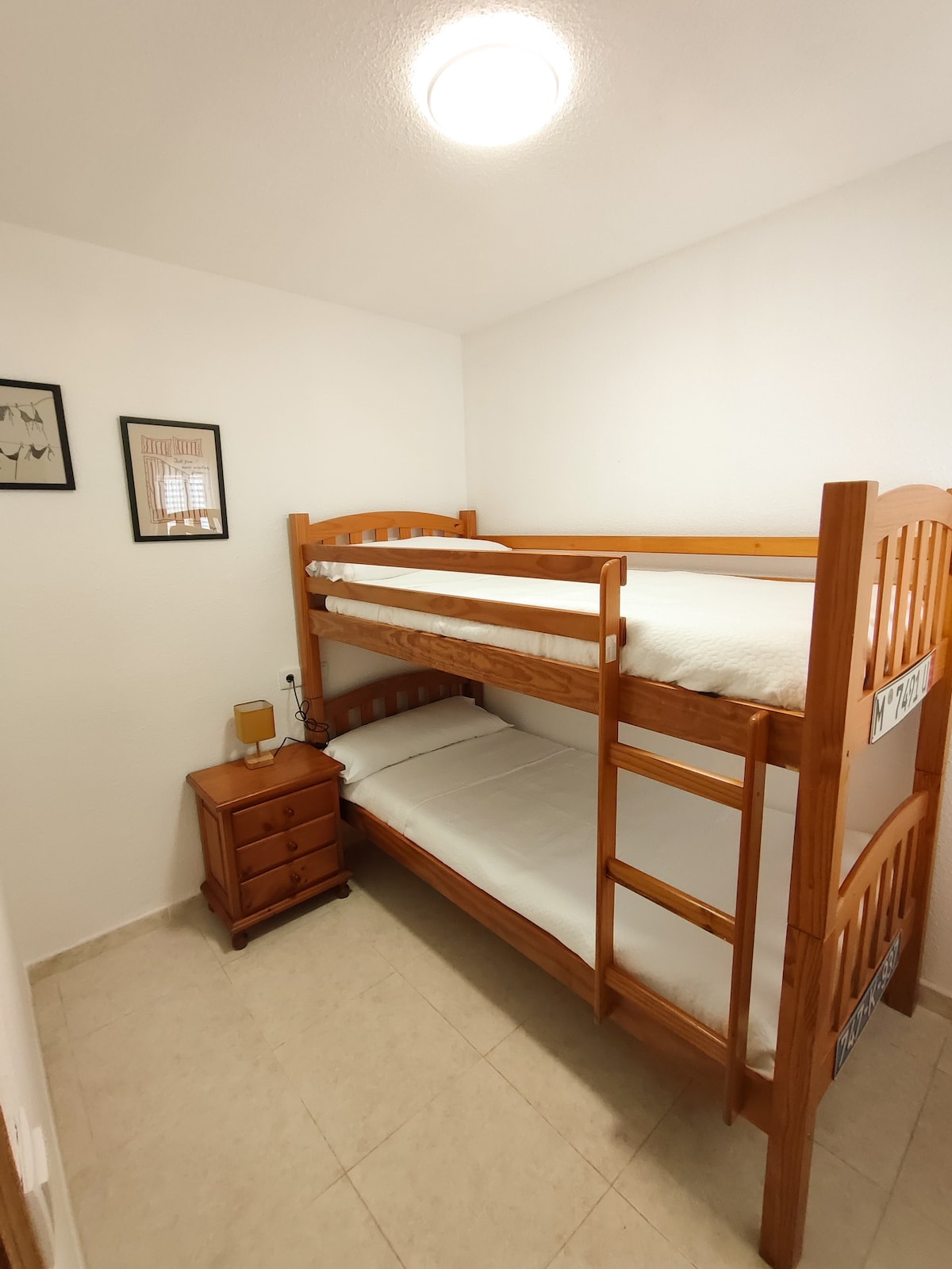 غرفة نوم بسريرين بطابقين 90 سم. يحتوي على طاولة بجانب السرير ومريحة.