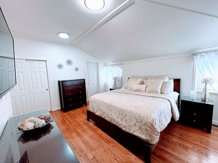 חדר שינה ראשי עם מיטת קינג סייז בסגנון קליפורני, טלוויזיה חכמה עם מסך שטוח וחדר רחצה צמוד. 