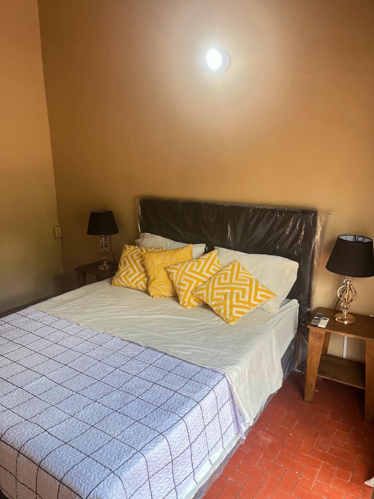 A well-appointed sleeping area features a spacious bed adorned with decorative yellow pillows. Two bedside tables with stylish black lamps provide additional lighting. Warm light emanates from a ceiling fixture, highlighting the neutral wall color and creating a cozy atmosphere.