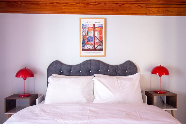 Svijetla spavaća soba s modernim crvenim svjetiljkama i mekim tapeciranim uzglavljem.