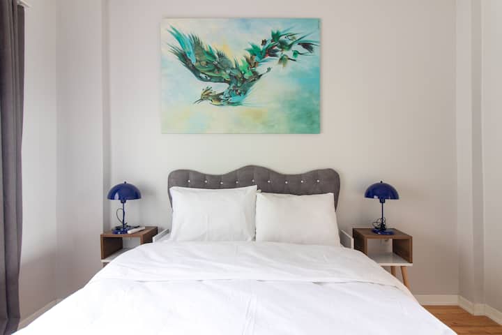 Svijetla spavaća soba s bračnim krevetom (160x200) i umirujućim umjetničkim radovima na zidovima.