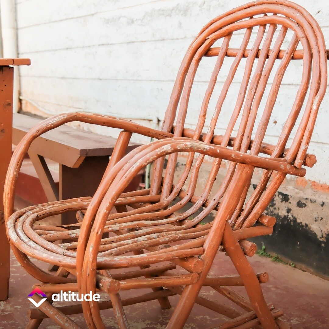 An intricately crafted wooden chair is displayed, showcasing a natural, rustic aesthetic. The chair's design features curved slats and a sturdy frame, offering a comfortable seating option. A small wooden table is positioned nearby, complementing the overall arrangement.