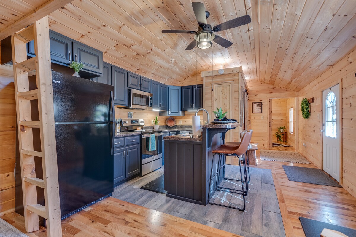 A well-equipped kitchen features dark cabinetry and stainless steel appliances, including a refrigerator and stovetop. A central island offers seating for two, complemented by wooden flooring that adds warmth. Natural light filters through a nearby door, enhancing the inviting atmosphere of this cozy retreat.
