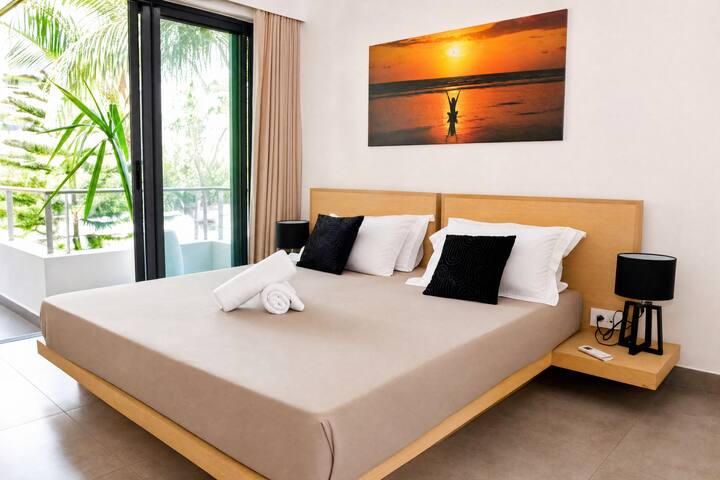 Chambre principale avec lit double 180x200, linge de qualité et serviettes préparées. Tête de lit en bois, grande fenêtre avec vue sur les palmiers de la résidence. Clim et rangements inclus.