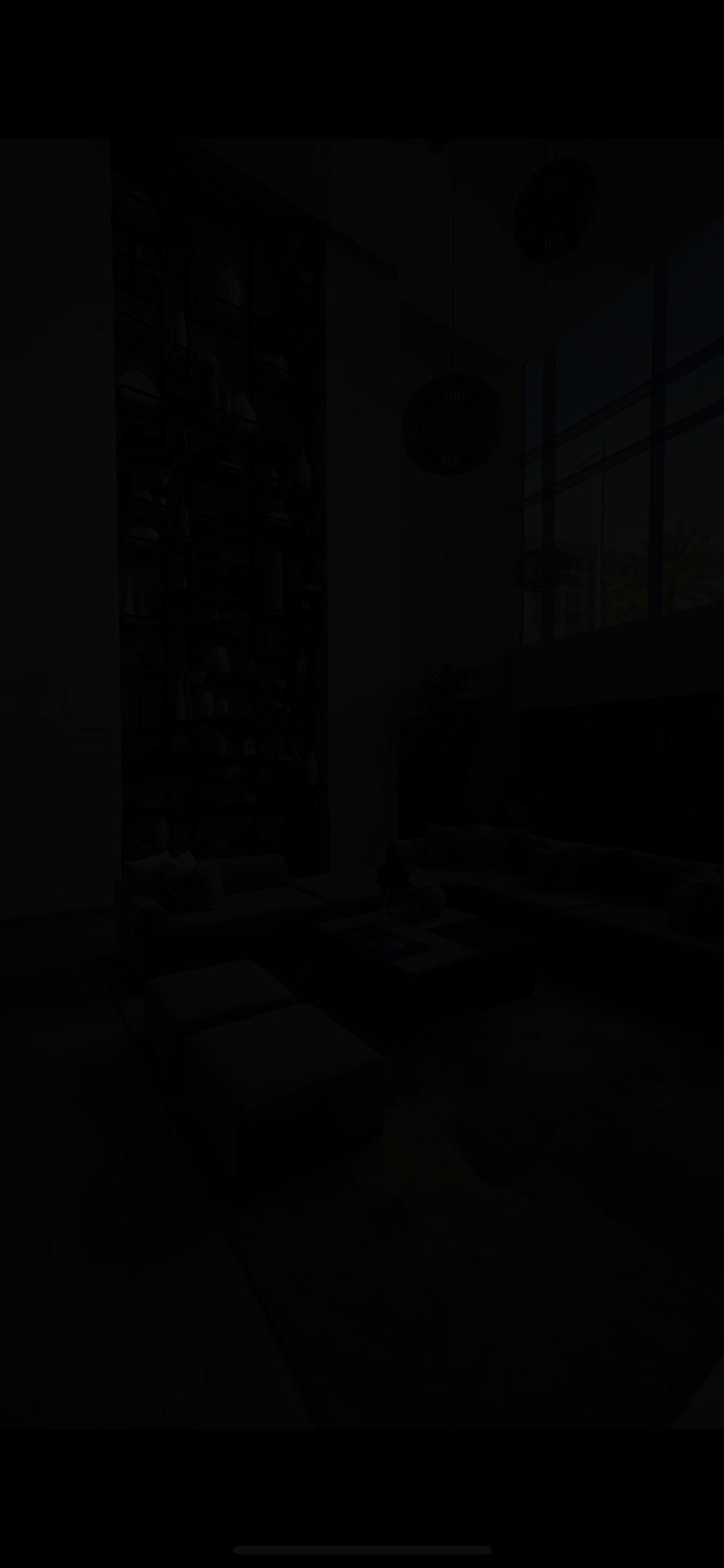 A spacious living area is presented, featuring large windows that allow natural light to fill the room. A plush seating arrangement is centered around a coffee table, and a tall shelf against the wall is lined with various decorative items.