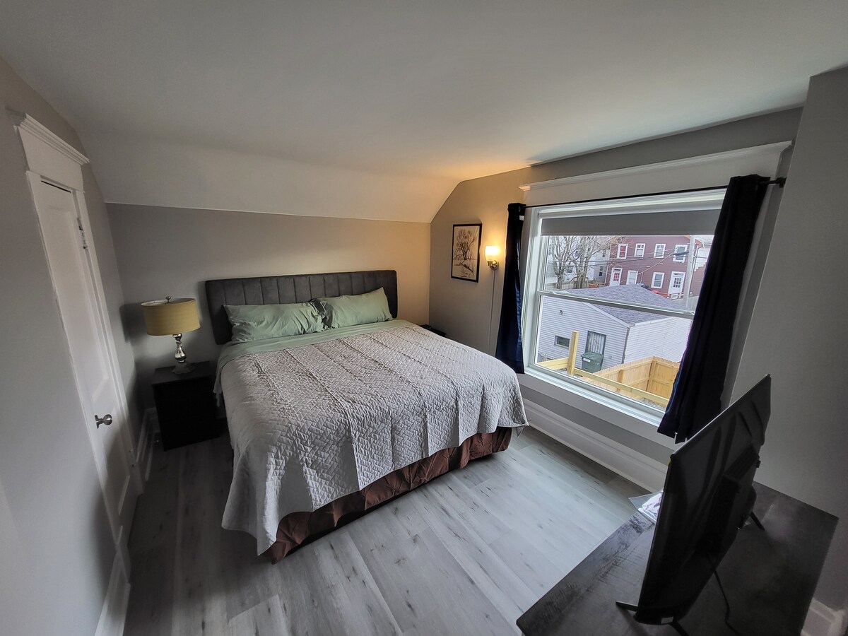 Dormitorio principal con cama tamaño king,  armario con perchas, TV de pantalla plana, sábanas limpias y persianas oscuras.