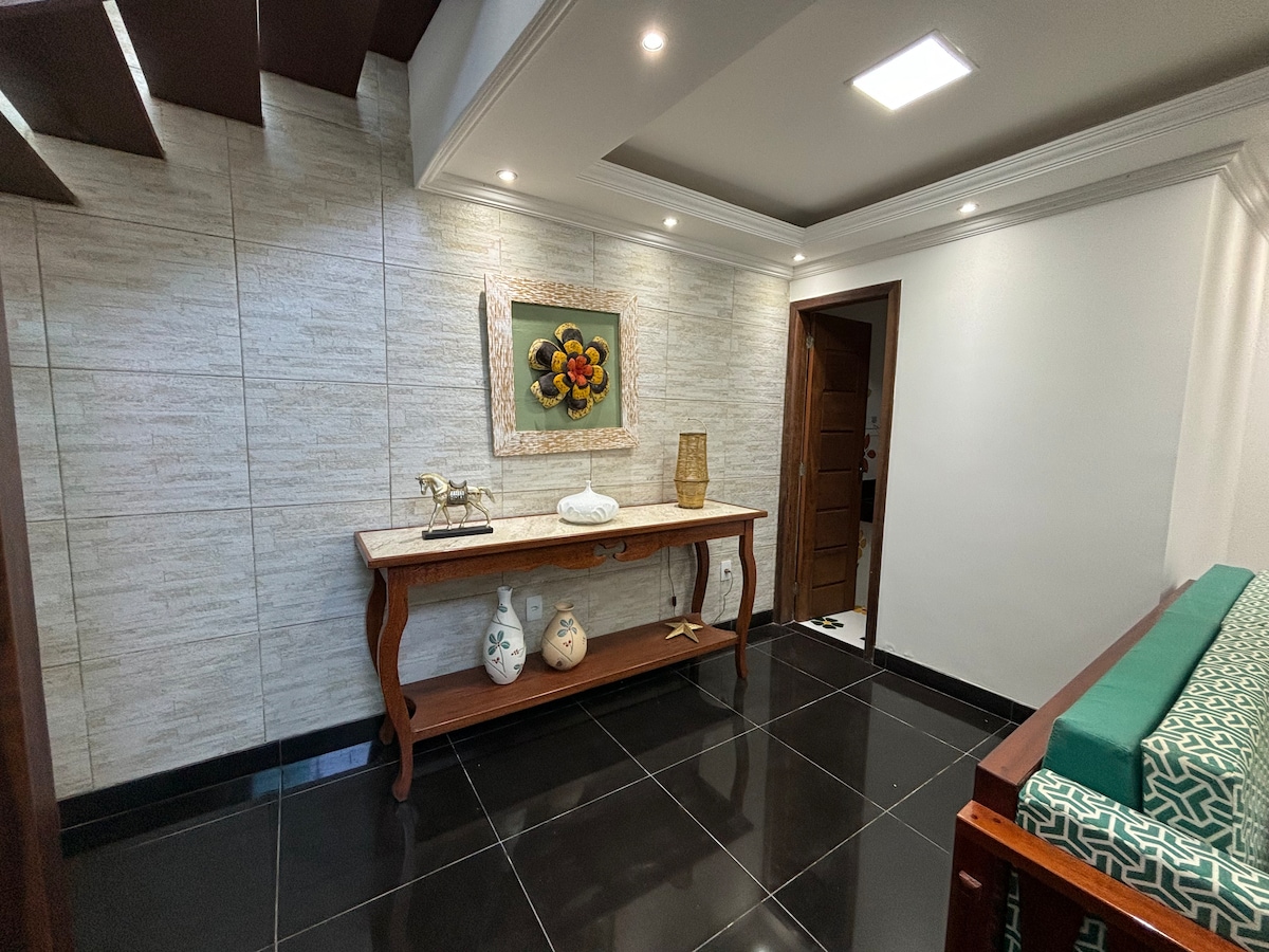 A welcoming entryway features a wooden console table with decorative items, including a vase and artwork. The sleek black tile floor contrasts with the light-colored walls, while soft lighting highlights the space. A wooden door provides access to other areas of the house.