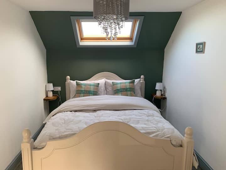 Relax in a king-size bed with quality bedding. The room includes a dressing table with drawers and chair, a hanging area for clothes, side shelving with lamps, and space to charge phones or place a monitor. Soft, high-quality towels are provided.
