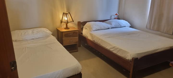 Svetlá a funkčná spálňa s manželskou posteľou a samostatným lôžkom
Je vybavený manželskou posteľou a samostatnou posteľou.
Je tu drevený komod na ukladanie oblečenia, pracovný stôl so stoličkou a ventilátor na udržanie chladnej atmosféry. 