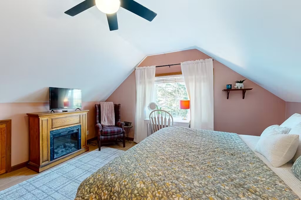 Rymligt sovrum med dubbelsäng, mysig öppen spis och gott om naturligt ljus. Perfekt för att koppla av efter en lång dag vid sjön.