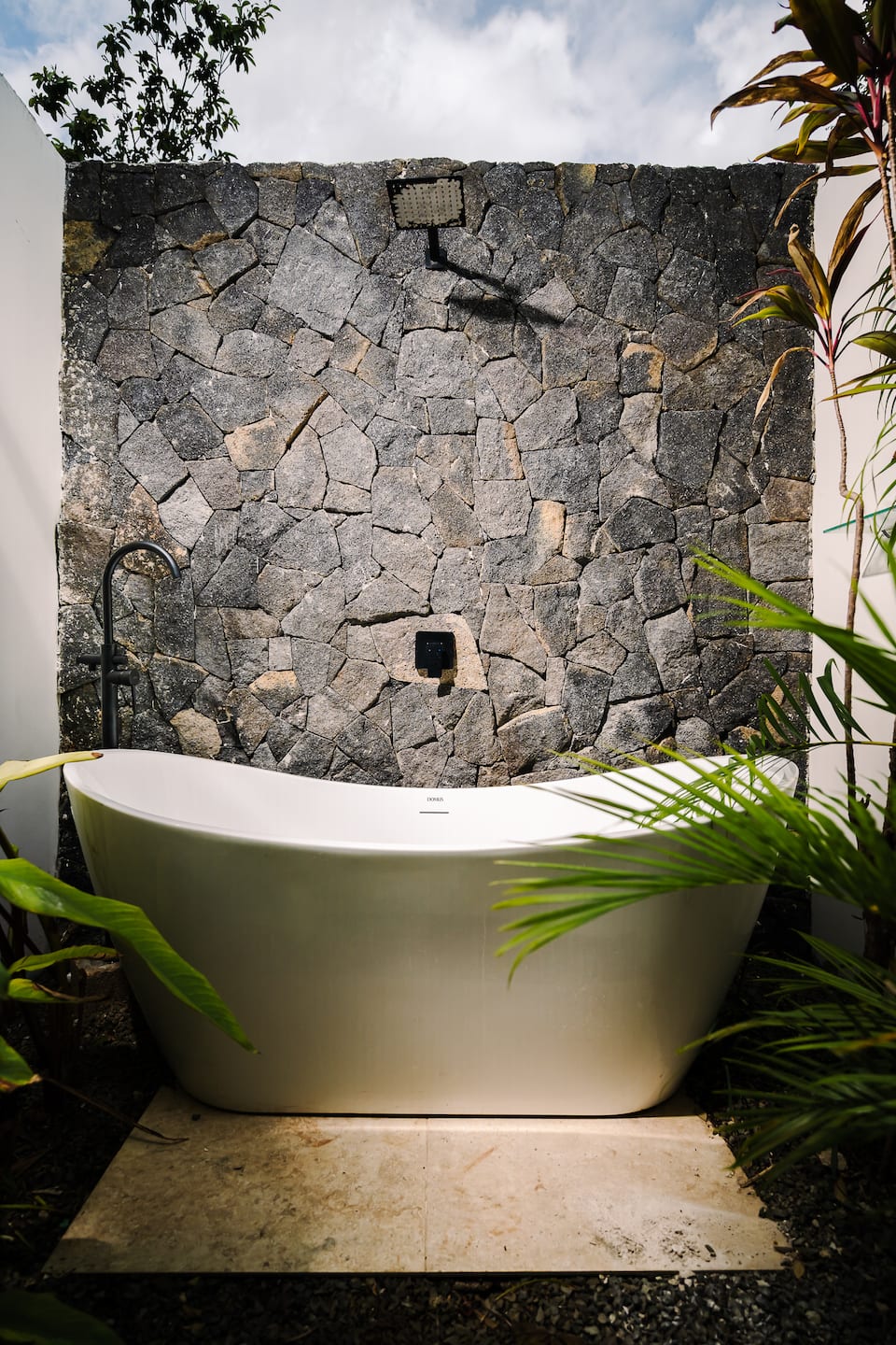 A freestanding tub against a stone wall, open to the sky