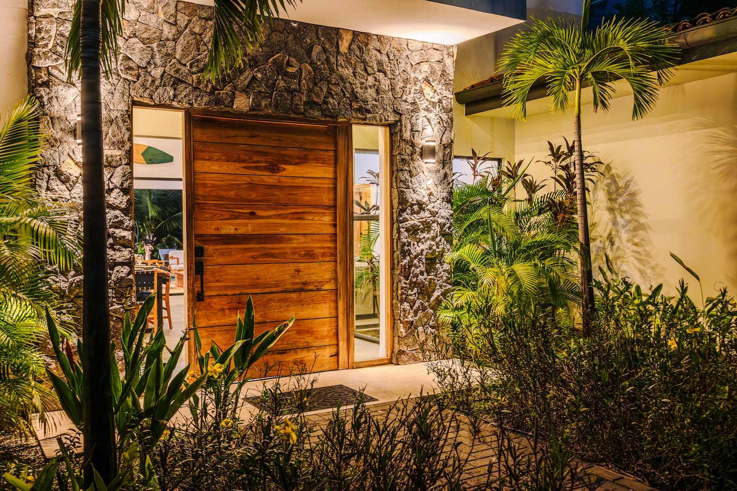 The wooden front door of Villa Reserva 101 at dusk, the garden lit