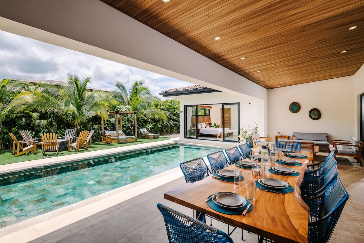 A long table under the wooden ceiling of the terrace, beside the pool