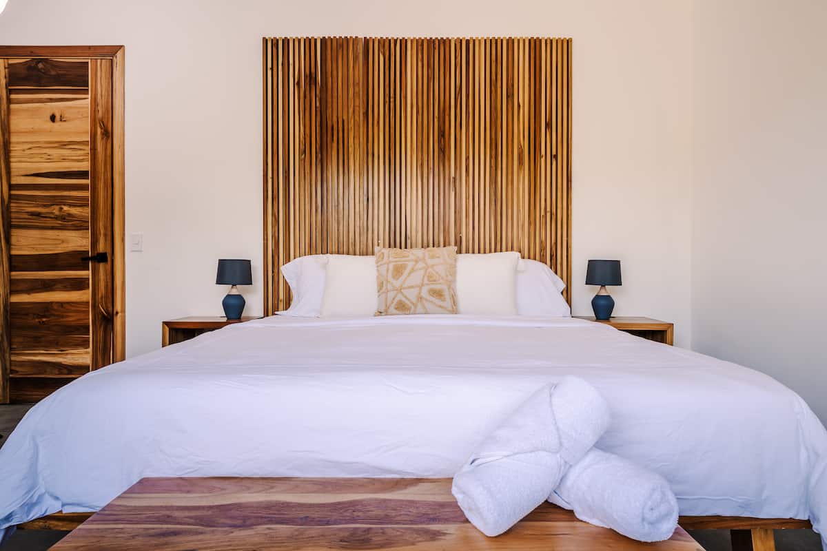 A made king bed with rolled towels against a wooden headboard