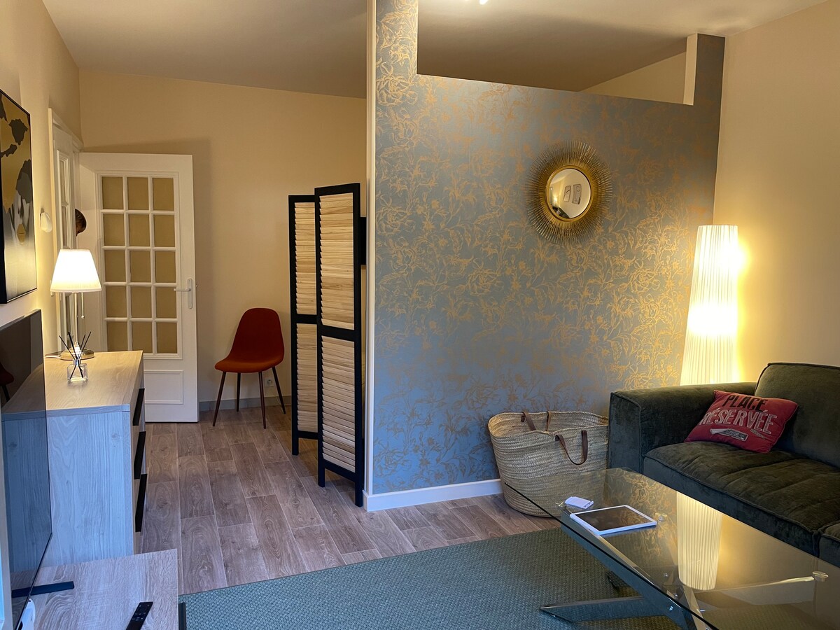 A well-arranged living area features a cozy sofa beside a glass coffee table. A floor lamp provides light, and a decorative mirror is mounted on the wall. A folding screen adds privacy, while a dining chair is visible in the corner next to a door with glass panels.