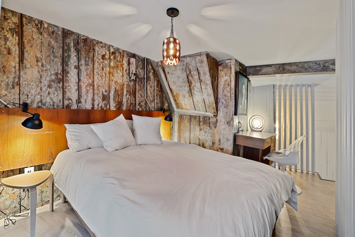 Полуотворена спалня с голямо двойно легло. Вертикално разположени греди разделят спалнята от всекидневната
