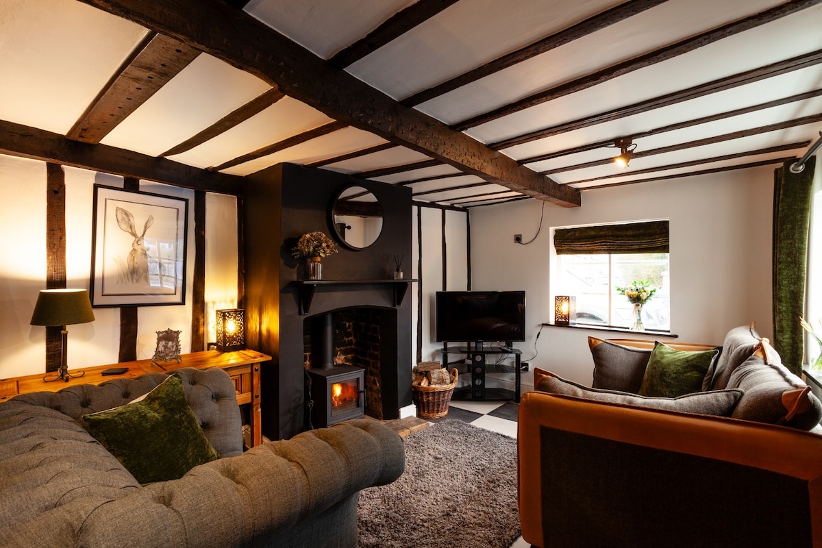 A comfortable living area features two distinct seating arrangements, one with a plush brown sofa and the other in gray upholstery. A modern television is positioned across from the seating, while a warm fireplace adds character to the space. Decorative lamps and a small table enhance the cozy atmosphere.