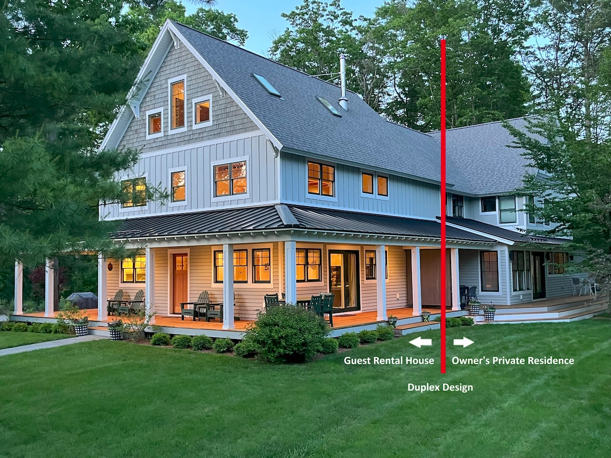 The image shows a modern duplex structure surrounded by lush greenery. The guest rental house features large windows that reflect warm light. A spacious covered porch with chairs is visible, enhancing the outdoor living space. The owner's private residence is indicated to the right.