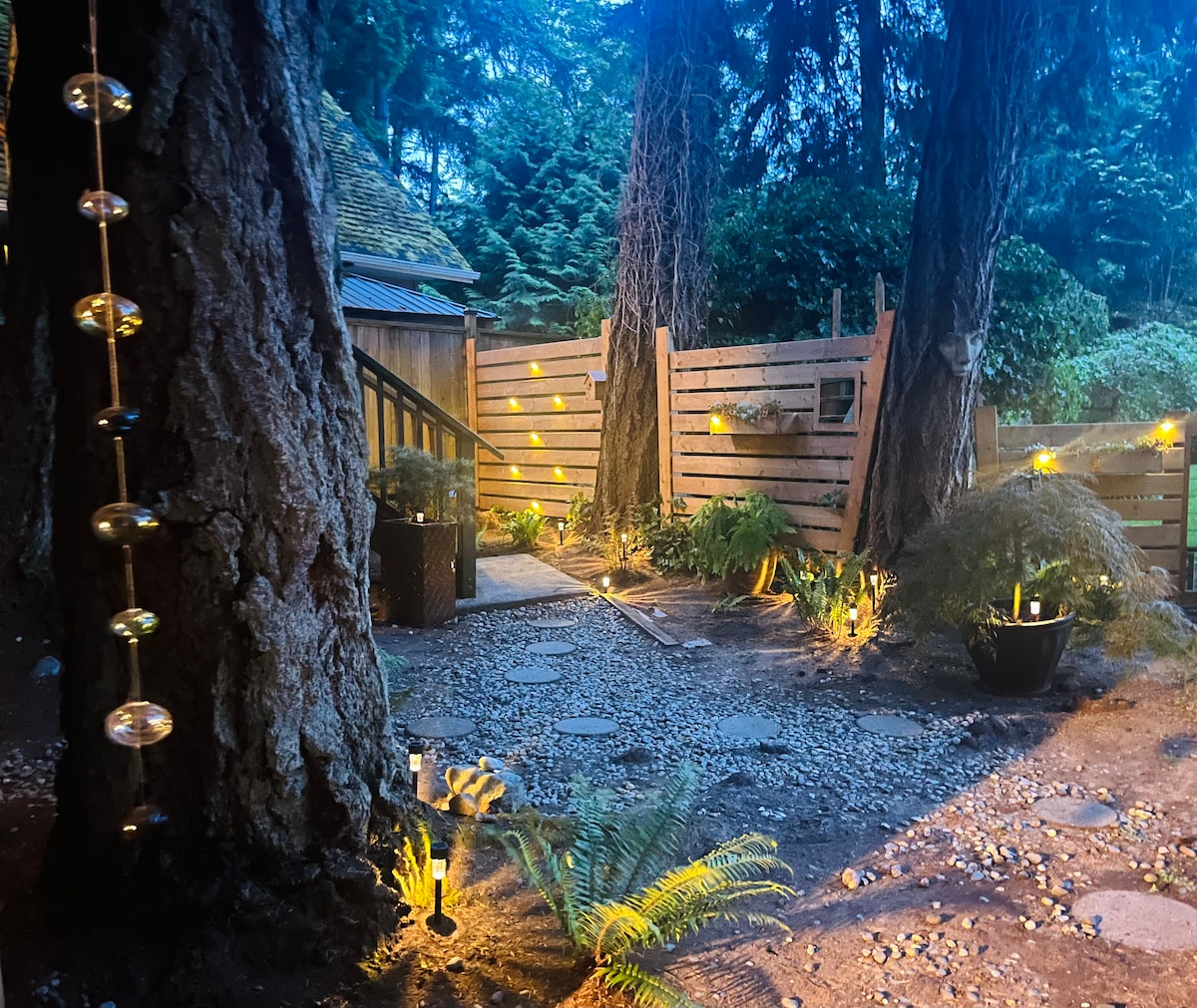 A tranquil outdoor pathway is lined with softly glowing lights, guiding the way through a serene garden ambiance. Tall trees frame the scene, while ferns and potted plants add natural elements, creating a welcoming atmosphere for relaxation and exploration.