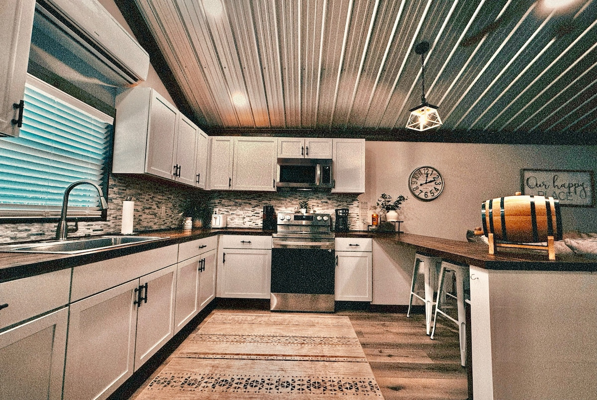 A well-organized kitchen showcases light-colored cabinets and a stylish backsplash. Stainless steel appliances provide a modern touch. A wooden countertop extends along one side, complemented by a decorative area rug. Natural light filters through a window, illuminating the space.