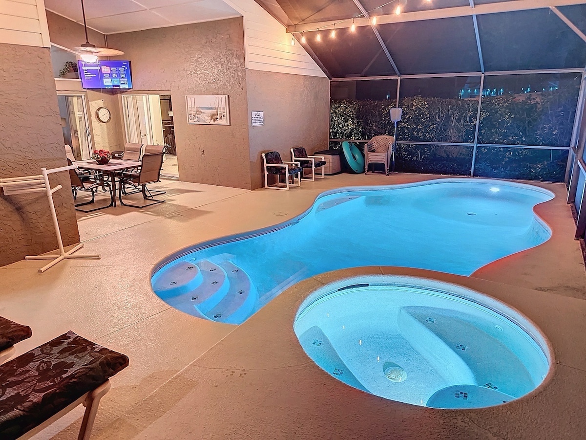 A private outdoor space features a sparkling pool and a rejuvenating spa, both illuminated with soft blue lights. Comfortable seating is arranged nearby, with a dining table set for relaxation. The screened enclosure provides a serene atmosphere, enhancing the experience of this inviting oasis.