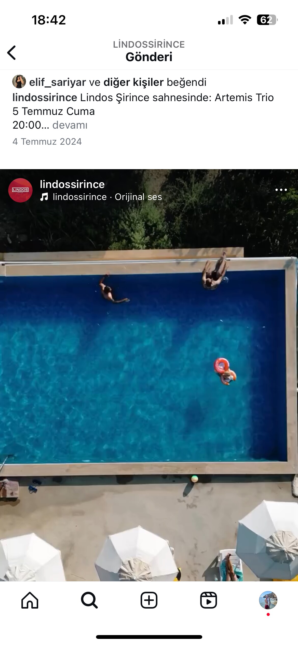 An aerial view captures a clear blue swimming pool surrounded by lounge chairs and umbrellas. Several individuals are seen enjoying the water, with some relaxing on floating inflatables. The pool area is framed by a serene outdoor setting.