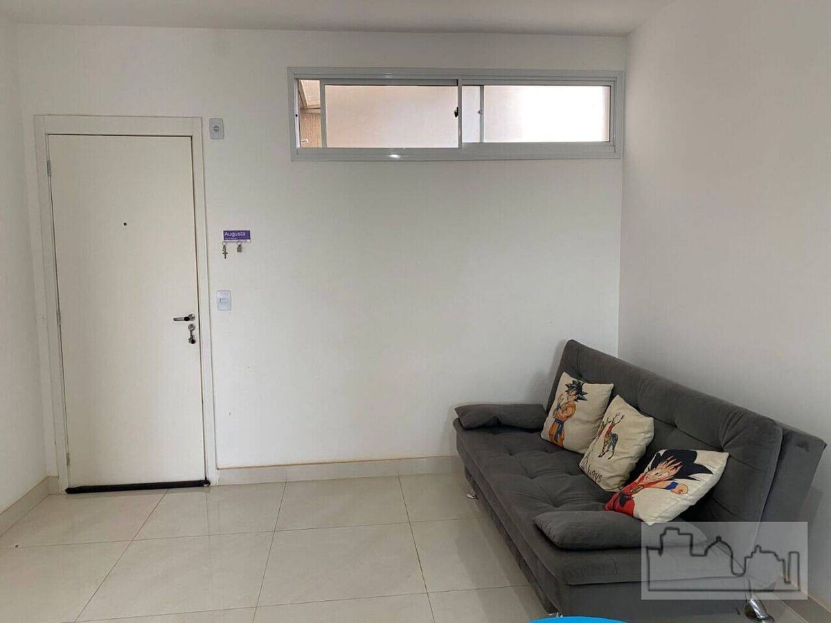 A light-filled living area features a grey sofa adorned with decorative pillows. A single, narrow window allows natural light to brighten the space. The walls are painted in a neutral tone, and a door leads to the outside, enhancing the room's accessibility.