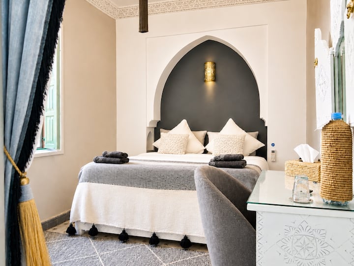 Chambre Kasbah avec lit Queen Size, dressing, bureau et vue extérieure. Climatisation, TV câblée, Wi-Fi haut débit, décoration marocaine élégante et confort au cœur de Marrakech.