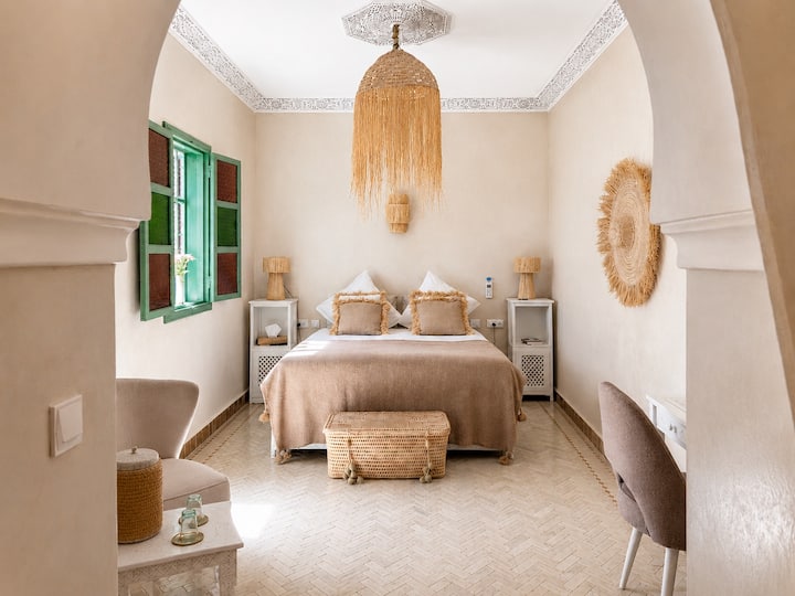 Suite élégante au style Chaabi chic aux tons beige, blanc cassé et caramel, zellige, coin salon, bureau/coiffeuse, rangements. Salle de bain privative, vue piscine, Wi-Fi haut débit, TV câblée  pour un voyage unique dans la médina de Marrakech.
