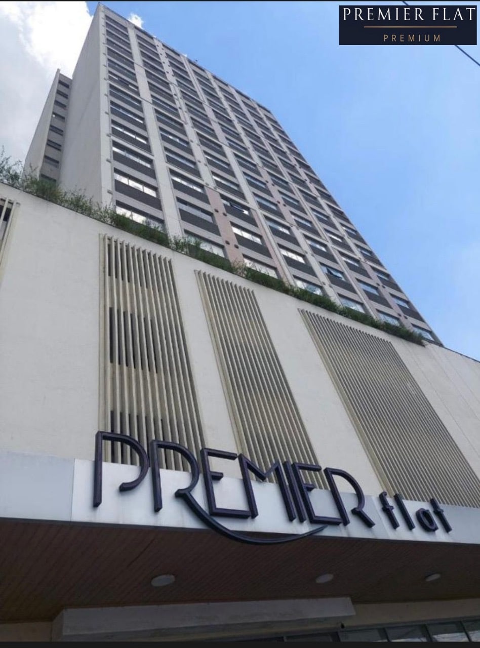 The exterior of a modern high-rise building is captured, showcasing a sleek design with vertical elements and a prominent sign that reads 'PREMIER flat.' The blue sky is visible above, providing contrast to the architectural details.