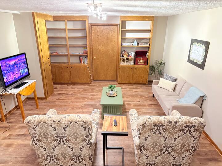 Obývacia izba s konferenčným stolíkom, koncovým stolíkom, knihami, košíkom na hry, gramofónom a platňami, televízorom a diaľkovým ovládačom. 