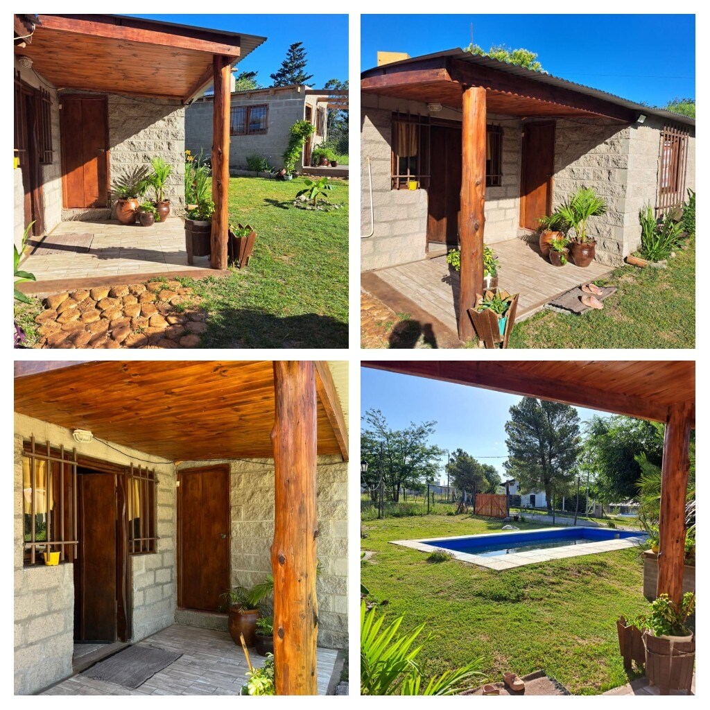 The exterior entrance features a wooden overhang supported by sturdy posts, welcoming guests to the stone facade of the cabin. Surrounding greenery enhances the outdoor space, and a view of a swimming pool can be seen in the background, inviting relaxation.