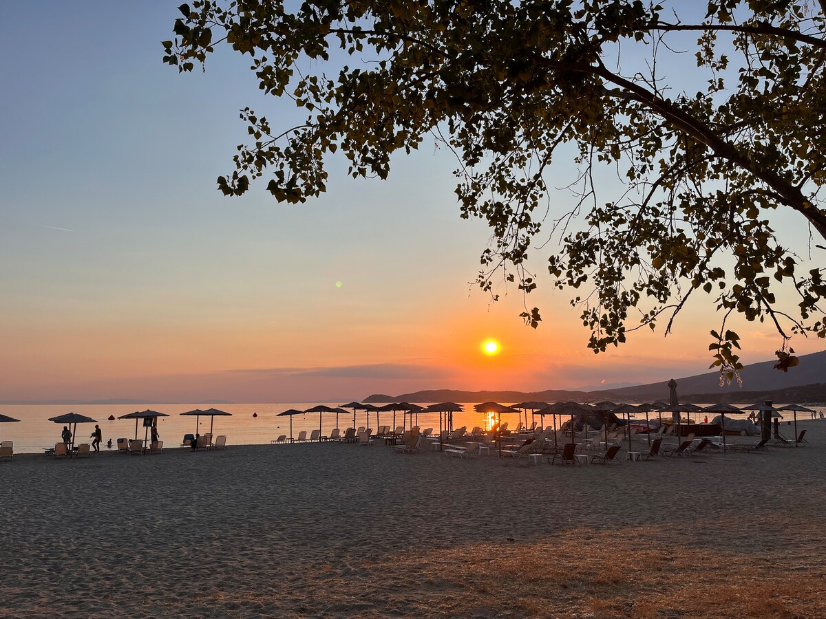 A serene beach scene is captured at sunset, showcasing gentle waves and a warm color palette. Several umbrellas are arranged neatly on the sandy shore, alongside lounge chairs. The horizon reflects hues of orange and pink, creating a calming atmosphere free of distractions.